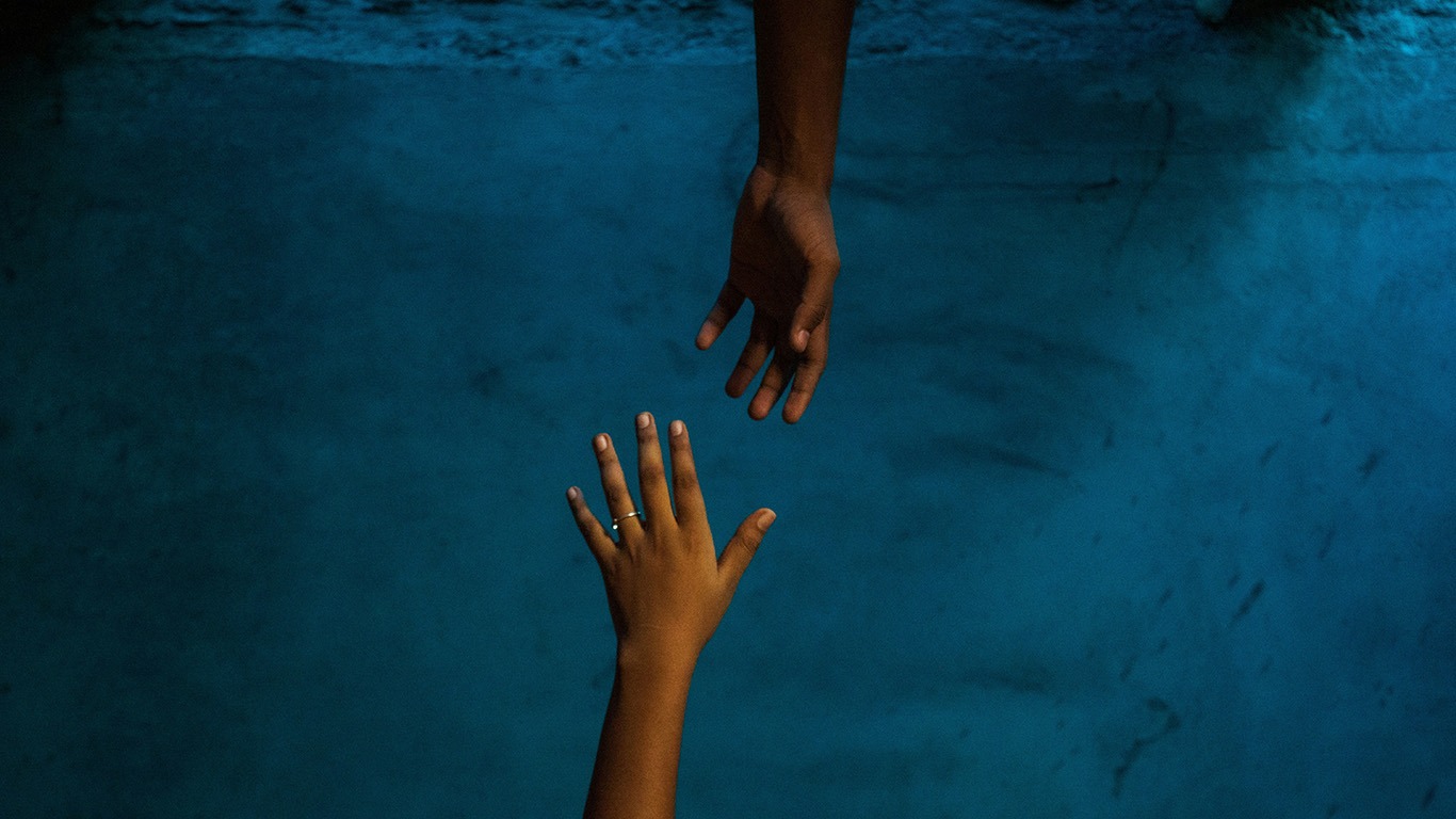deux mains tendues l’une vers l’autre sur fond bleu
