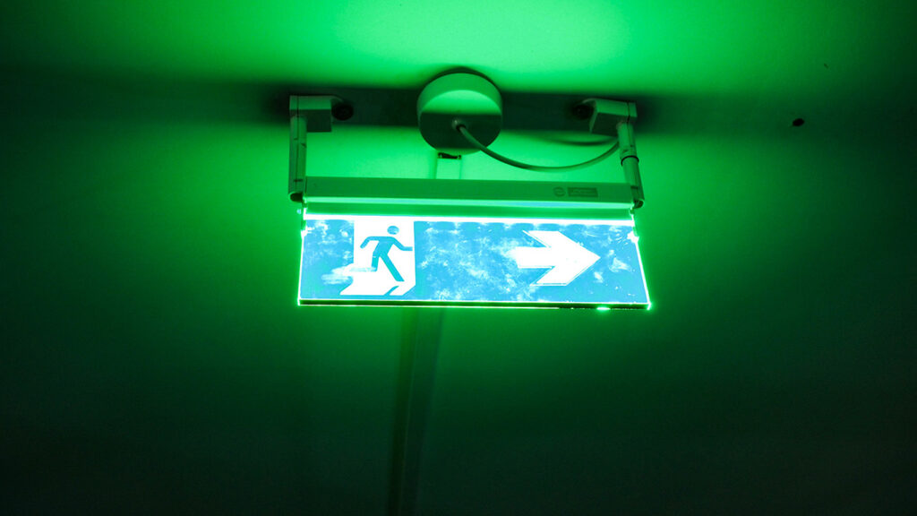 signalétique de sortie de secours verte accroché au plafond sous lumière de néon