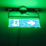 signalétique de sortie de secours verte accroché au plafond sous lumière de néon